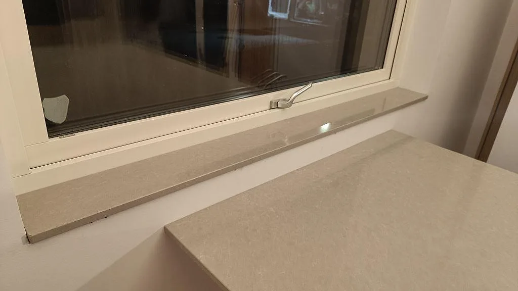 Fönsterbänk och bänkskiva i ljus polerad Technistone Noble Ivory White kvartskomposit vid köksfönster i Trelleborg.