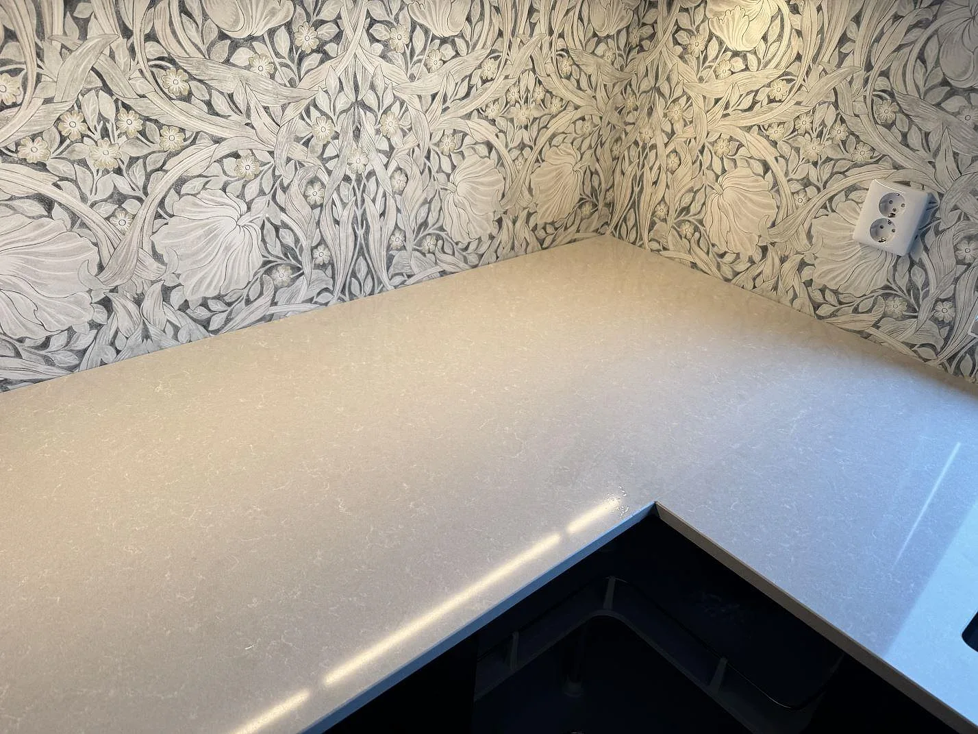 Polerad bänkskiva i Technistone Noble Ivory White, ljus kvartskomposit, som möter en mönstrad köksvägg i hörnet i Trelleborg.
