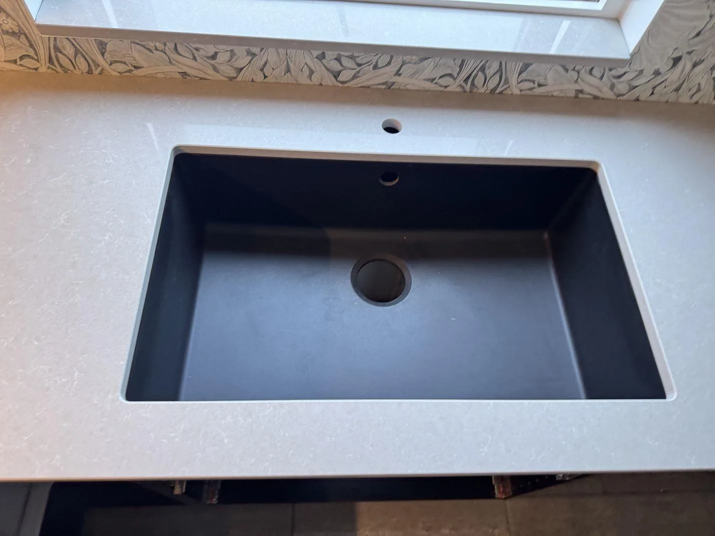 Närbild på mörk diskho i en polerad köksbänkskiva av Technistone Noble Ivory White, ljus kvartskomposit, under fönstret i Trelleborg.