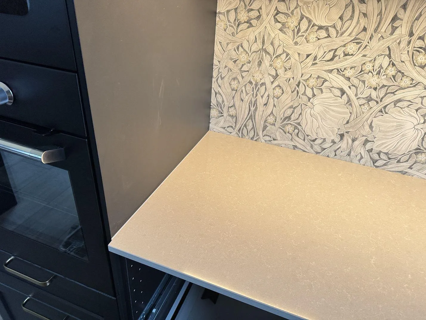 Köksbänk i Technistone Noble Ivory White, polerad kvartskomposit, bredvid svart ugn och mönstrad vägg i ett kök i Trelleborg.
