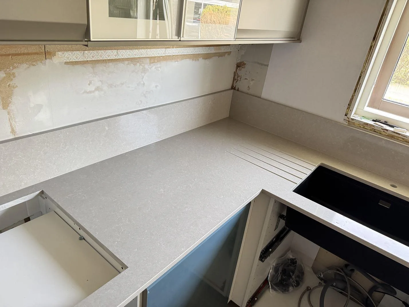 Polerad köksbänkskiva i Technistone Noble Ivory White med underlimmad mörk diskho, avrinningsspår och stänkkant i Trollhättan.
