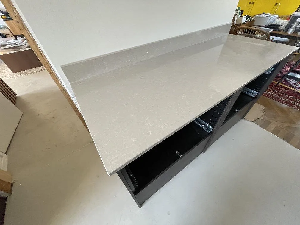 Lång arbetsyta i polerad Technistone Noble Ivory White komposit med låg stänkkant och mörka köksstommar i Tyresö.
