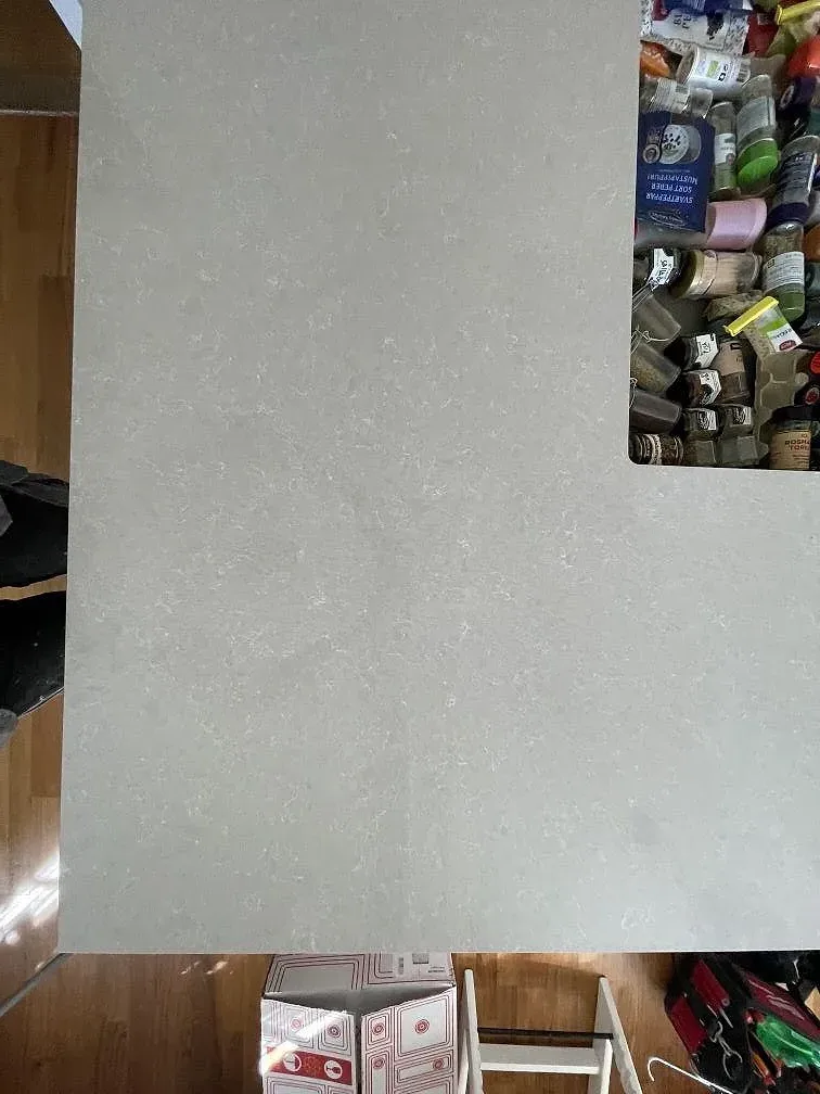 Köksö med bänkskiva i polerad Technistone Noble Ivory White, sedd ovanifrån med den molniga gråbeige strukturen i ett kök i Tyresö.