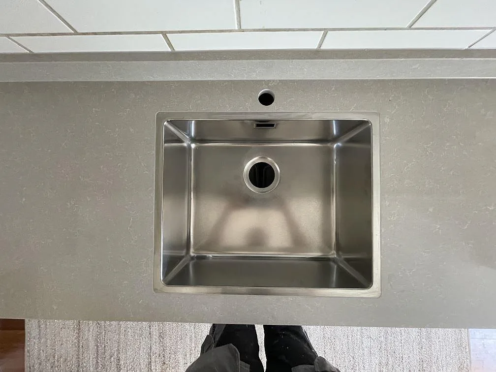 Underlimmad rostfri diskho i en köksbänkskiva av Technistone Noble Ivory White med ett blandarhål och vitt tegelstänkskydd i Tyresö.