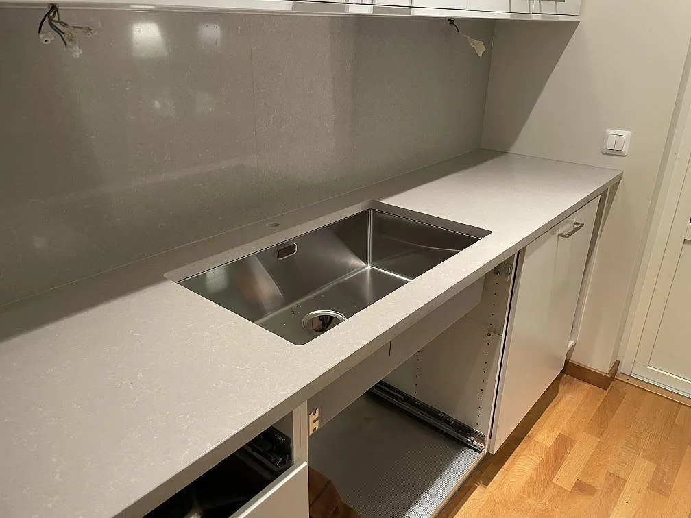 Diskhoområde i polerad Technistone Noble Ivory White, ljus kvartskomposit, med rostfri diskho och väggpanel i ett kök i Uppsala.