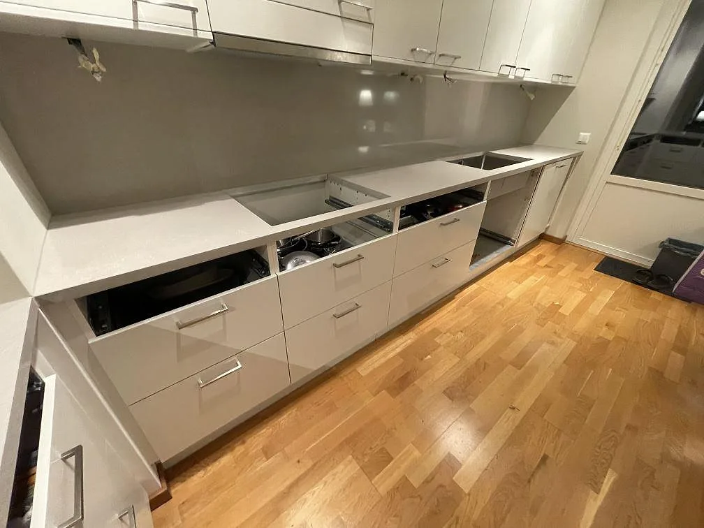 Lång köksbänk i polerad Technistone Noble Ivory White, kvartskomposit, med synliga urtag och grå vägg bakom bänken i Uppsala.