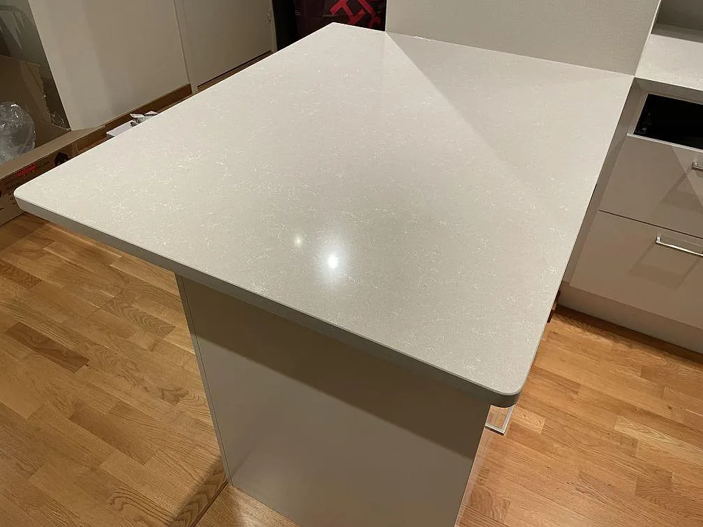 Halvö i polerad Technistone Noble Ivory White, ljus kvartskomposit, med rundade hörn och blank yta i ett kök i Uppsala.