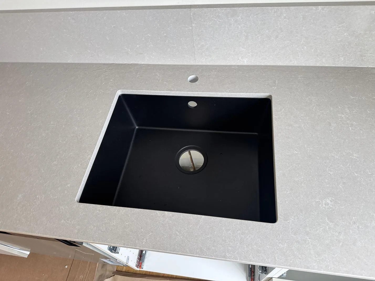 Närbild på svart diskho i polerad Technistone Noble Ivory White, kvartskomposit, med blandarhål bakom i ett kök i Vänersborg.