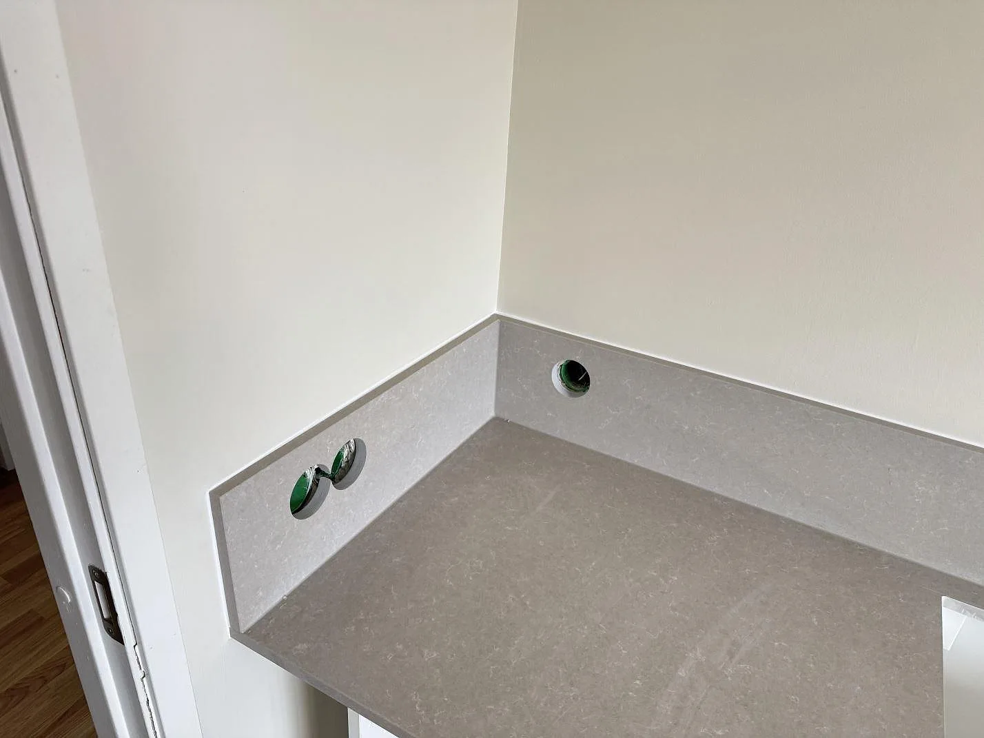 Detalj av låg stänkkant i Technistone Noble Ivory White, polerad kvartskomposit, med runda genomföringar i köket i Vänersborg.