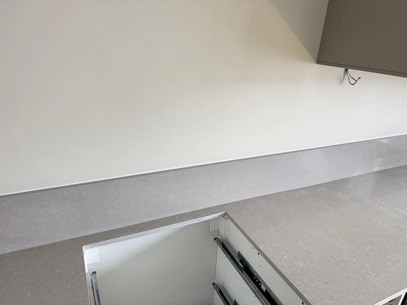Lång arbetsyta i polerad Technistone Noble Ivory White, kvartskomposit, med hällurtag och öppen köksstomme under montering i Vänersborg.