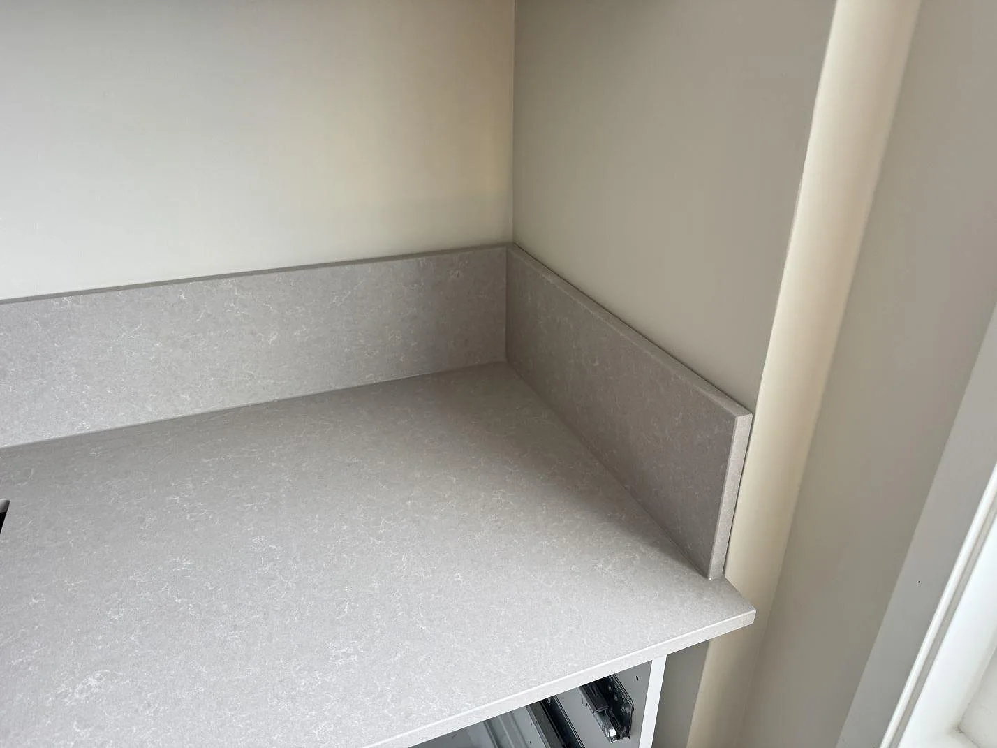 Hörnsektion av polerad köksbänkskiva i Technistone Noble Ivory White med matchande låg stänkkant vid fönster i Vänersborg.