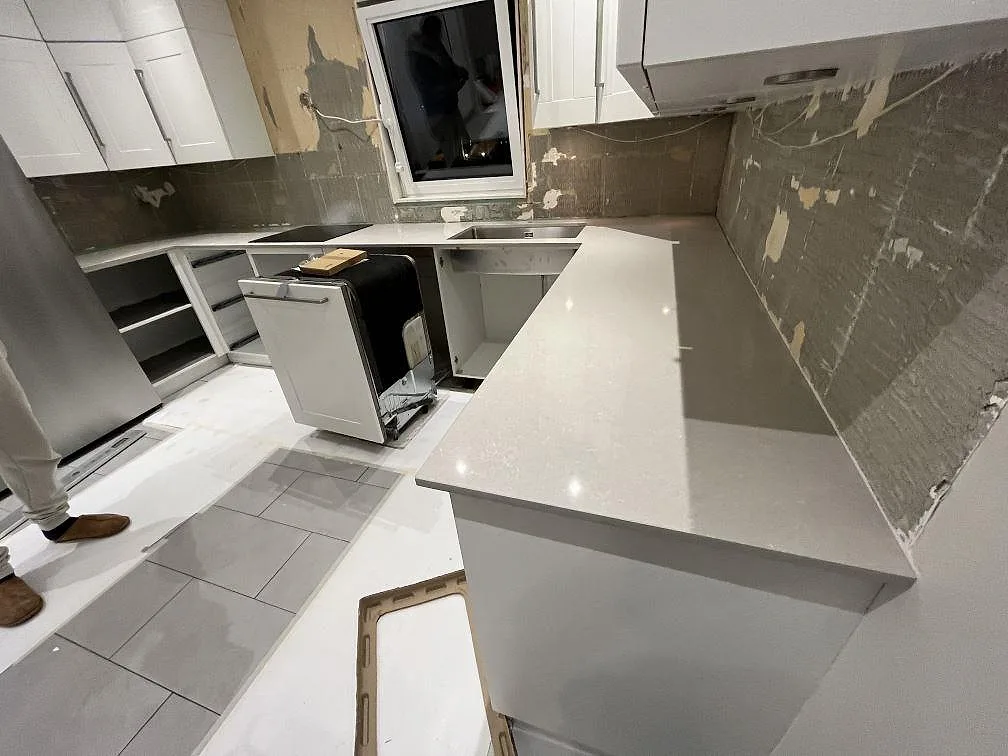 U-formad köksbänkskiva i polerad Technistone Noble Ivory White, 20 mm kvartskomposit, med halvö i ett kök under montering i Västerås.