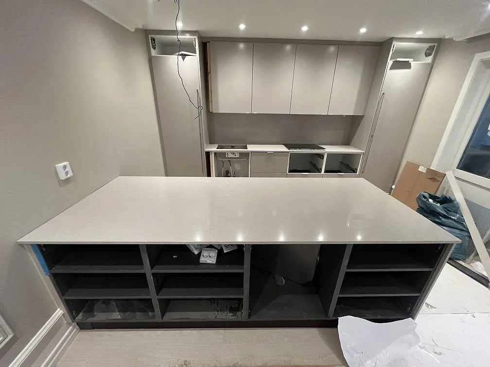 Köksbänkskiva i ljus Technistone Noble Ivory White, polerad kvartskomposit, på stor köksö och väggbänk under montering i Västerås.