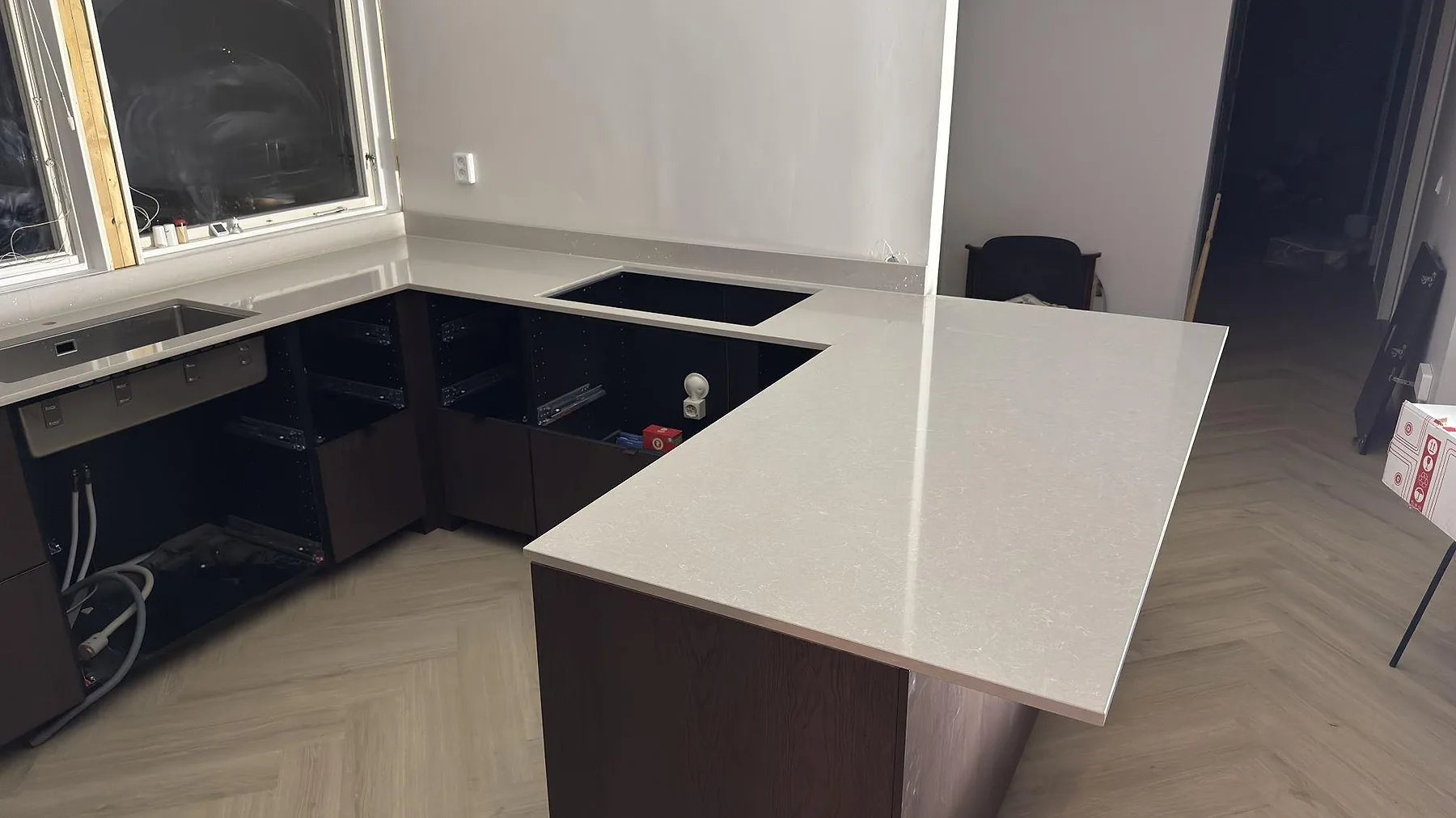 Polerad bänkskiva i Technistone Noble Ivory White med halvö och urtagning för häll, monterad mot mörka köksstommar i Västerhaninge.