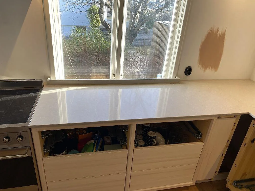 Ljus kvartskompositbänk i Technistone Noble Ivory White med låg bakkant och fristående spis intill i Västra Frölunda.