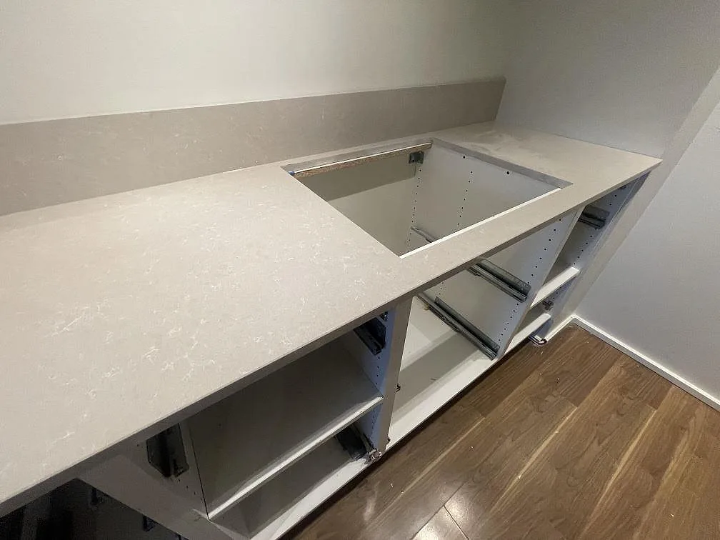 Detalj av hällöppning i polerad Technistone Noble Ivory White med låg stänkkant över öppna köksstommar i Vallentuna.