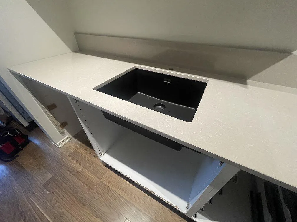 Närbild på svart diskho i köksbänkskiva av polerad Technistone Noble Ivory White med uppvikt stänkkant i Vallentuna.