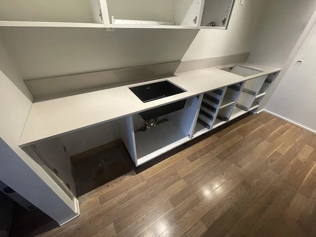 Lång köksbänkskiva i polerad Technistone Noble Ivory White med låg stänkkant, svart diskho och hällöppning i Vallentuna.