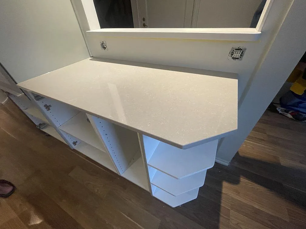 Vinklad bänkdel i polerad Technistone Noble Ivory White monterad vid fönster och öppna köksstommar i Vallentuna.