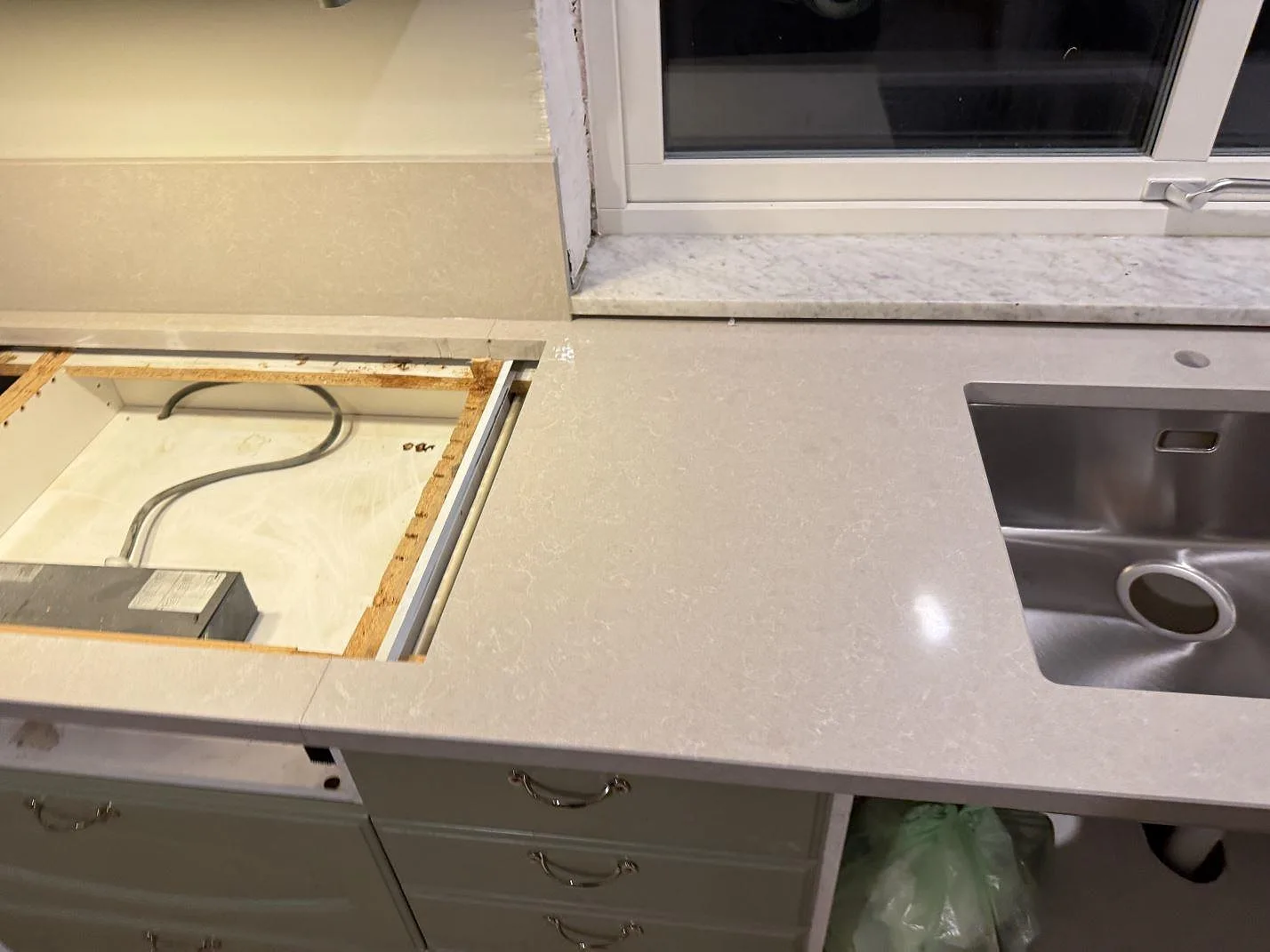 Köksbänkskiva i polerad Technistone Noble Ivory White med rostfri diskho, hällurtag och äldre fönsterbänk i ett kök i Veberöd.
