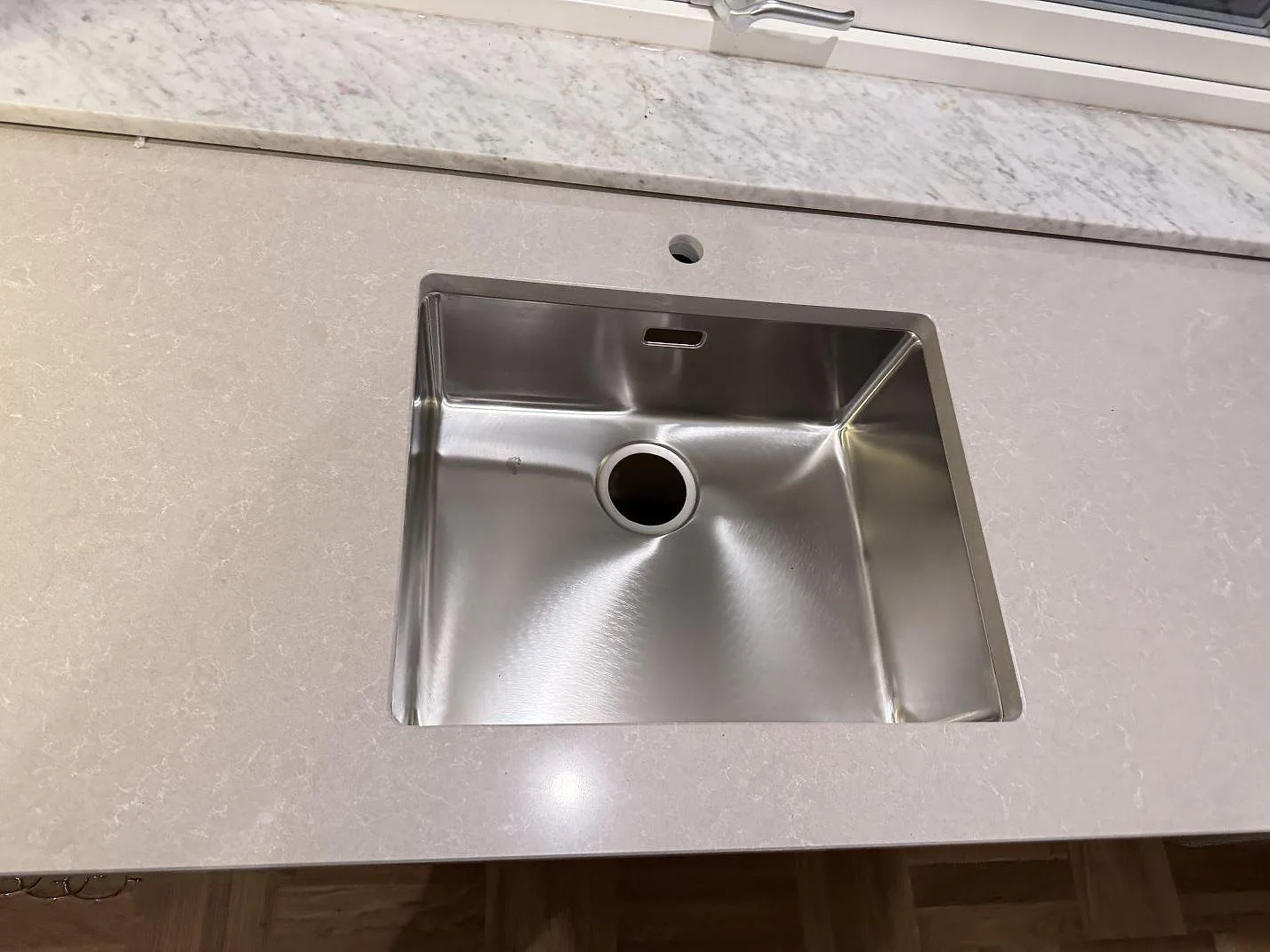 Närbild på underlimmad rostfri diskho i polerad Technistone Noble Ivory White, ljus kvartskomposit med blandarhål vid fönster i Veberöd.