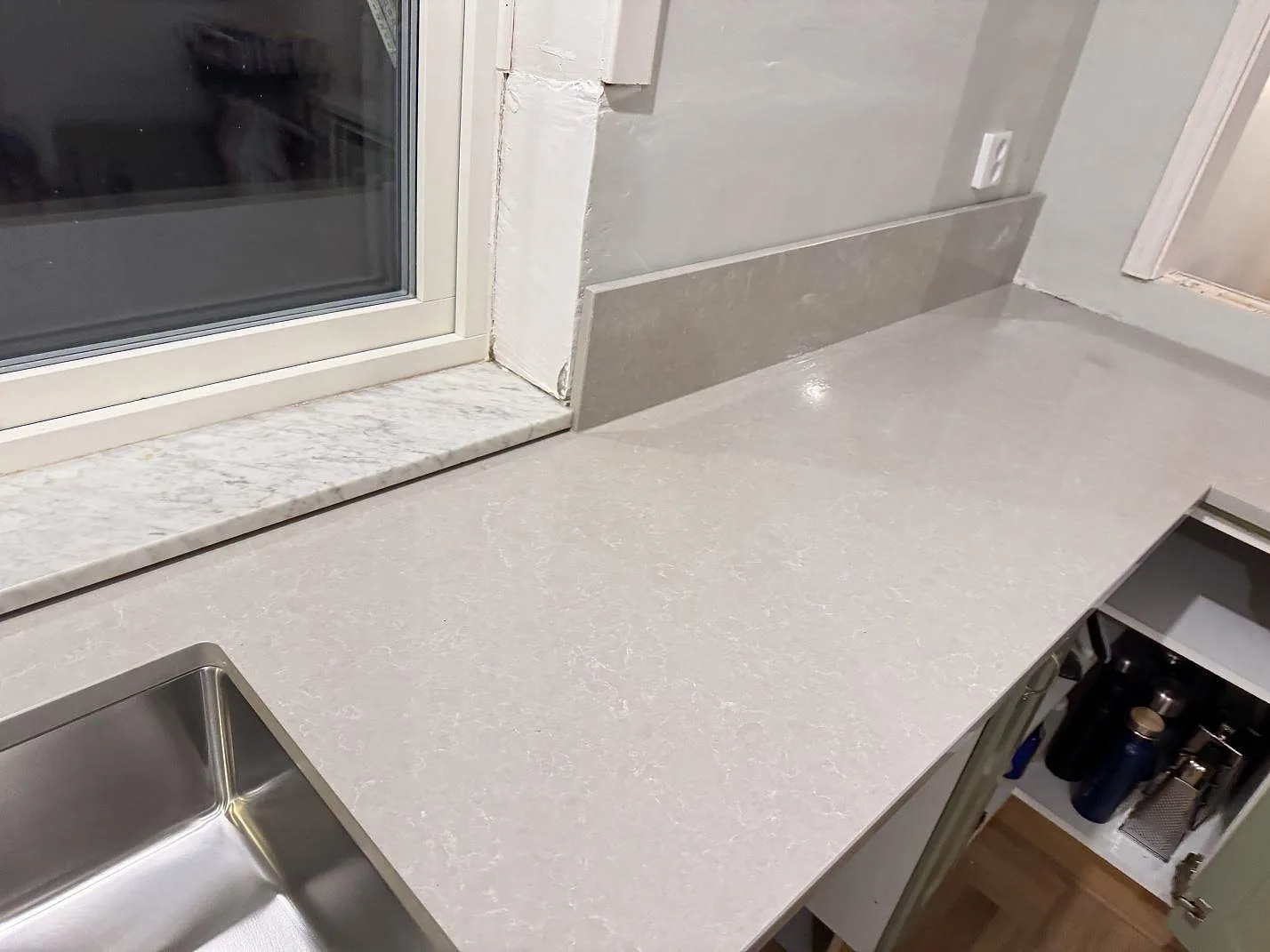 Polerad Technistone Noble Ivory White som köksbänkskiva i kvartskomposit vid fönster, med underlimmad rostfri diskho och låg stänkkant i Veberöd.