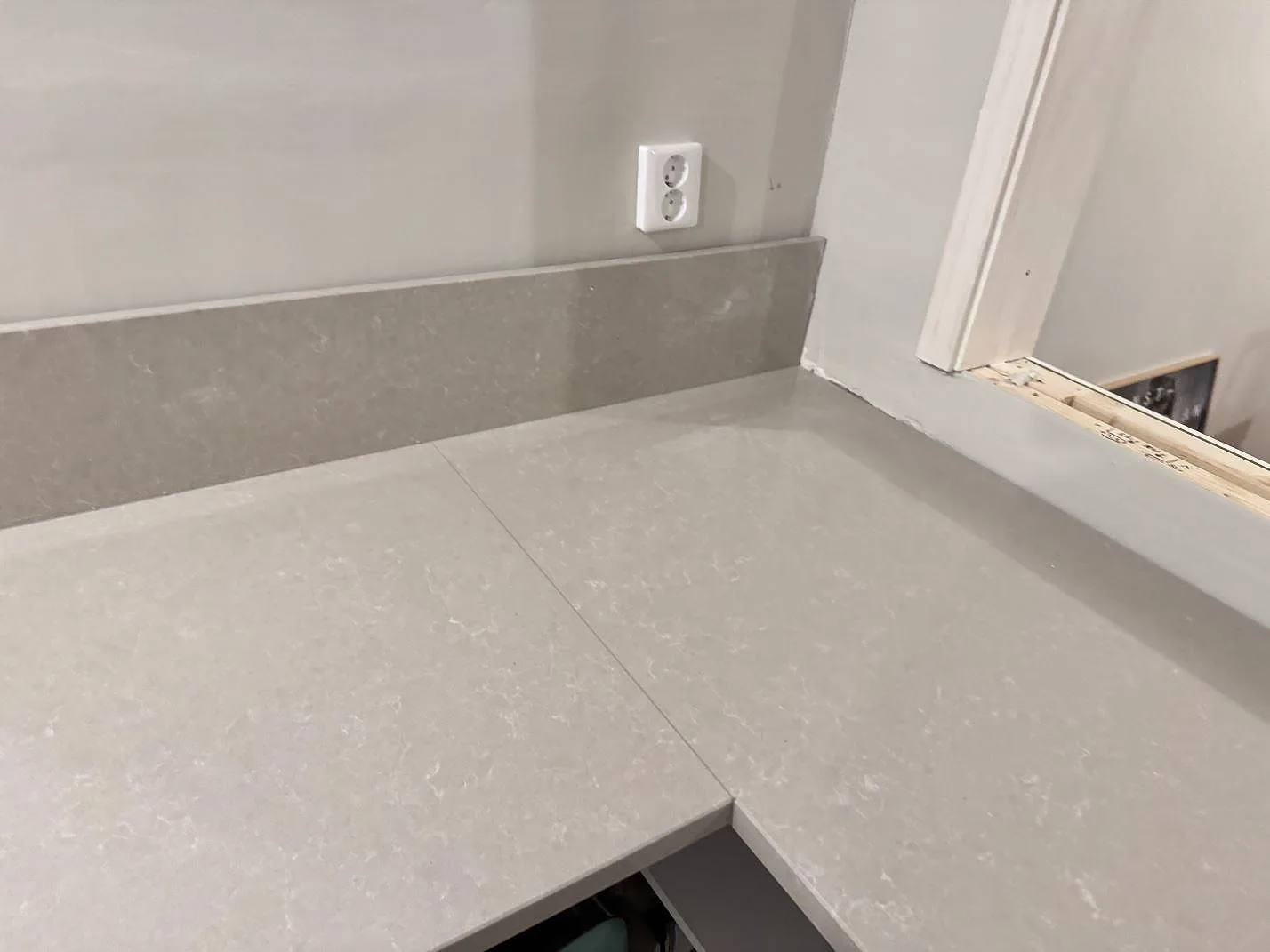 Hörnskarv och stänkkant i polerad Technistone Noble Ivory White, monterad som L-formad köksbänkskiva i ett kök i Veberöd.