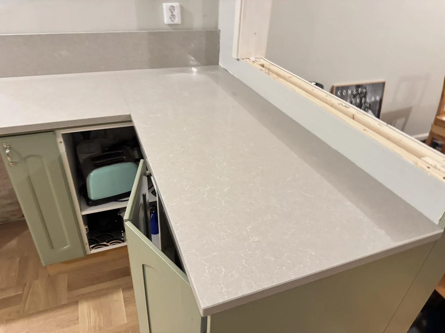 Höger arbetsyta i polerad Technistone Noble Ivory White, ljus kvartskomposit med stänkkant och gröna köksluckor under montering i Veberöd.