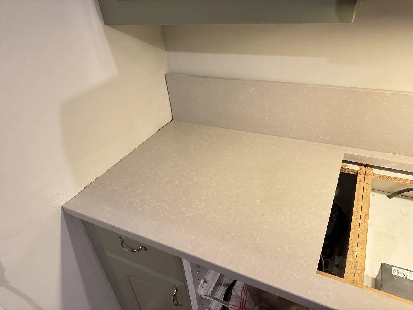 Väggbänk i polerad Technistone Noble Ivory White, ljus kvartskomposit med uppvikt stänkkant och hällurtag under montering i Veberöd.