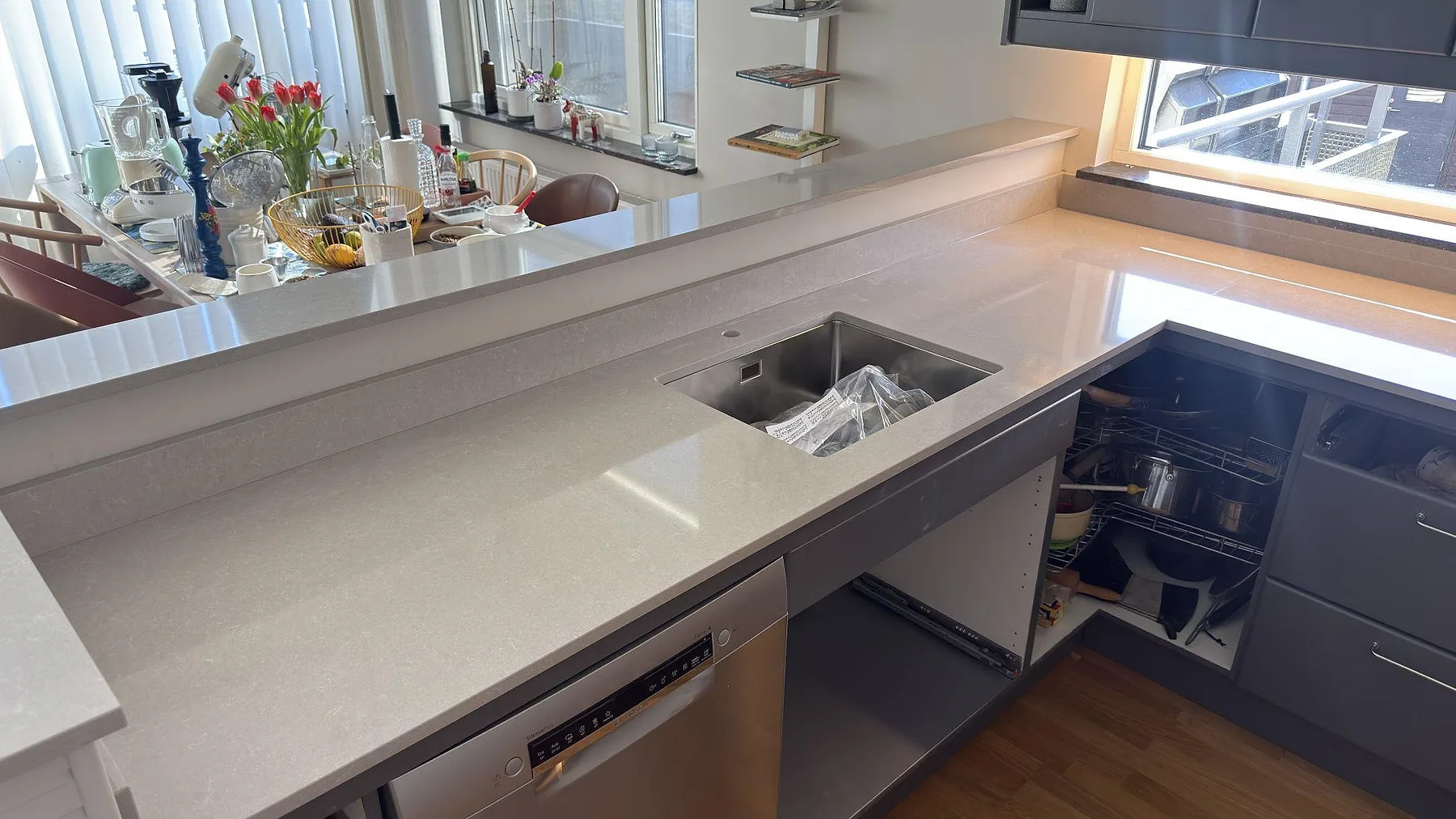 Halvö och bänkskiva i ljus Technistone Noble Ivory White i ett kök i Vega, med underlimmad rostfri diskho och rostfri diskmaskin.