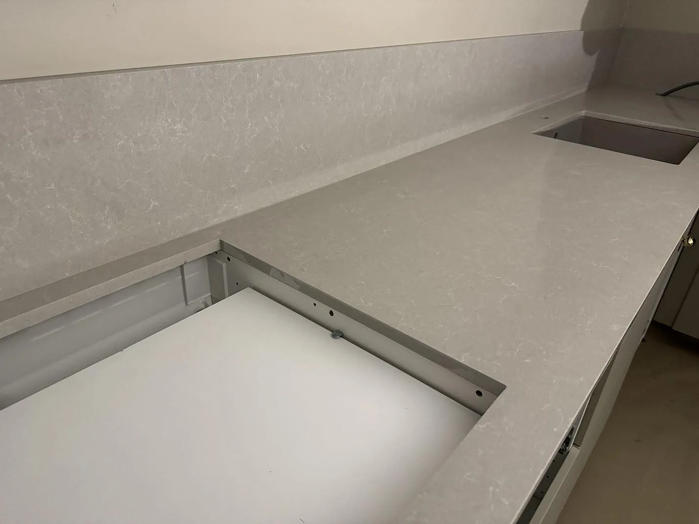 L-formad köksbänkskiva i Technistone Noble Ivory White, polerad komposit, med stänkskydd och hälluttag i Vellinge.