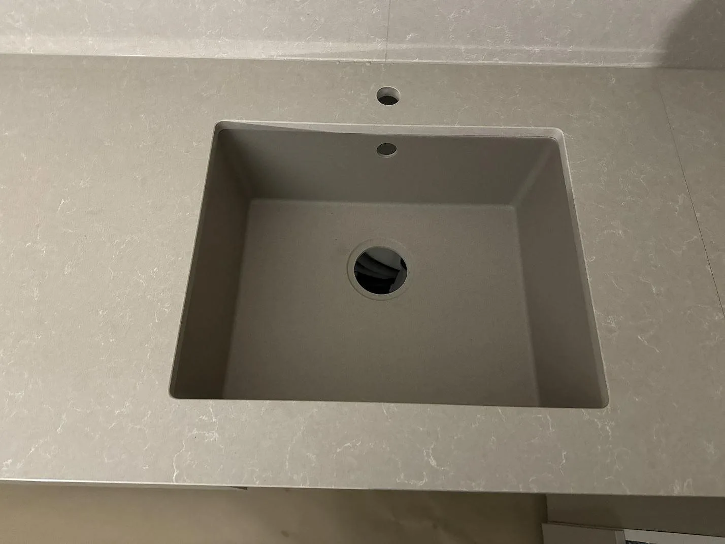 Närbild på underlimmad rostfri diskho i en köksbänkskiva av polerad Technistone Noble Ivory White i Vellinge.