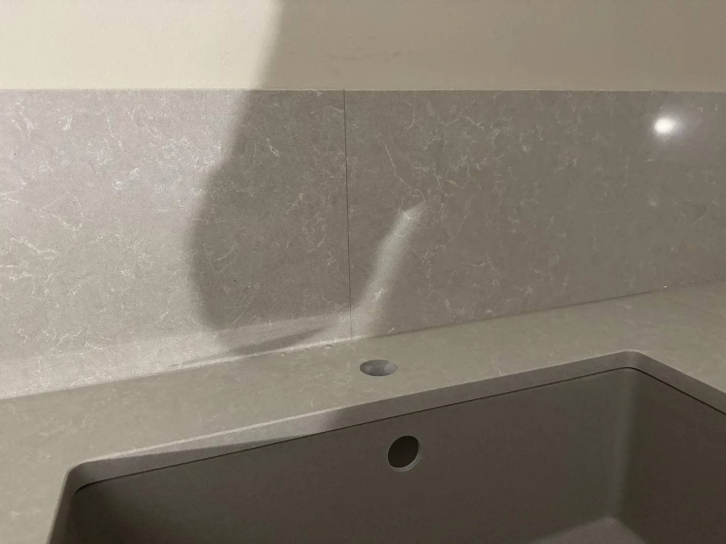 Närbild på stänkskydd och diskhozonen i polerad Technistone Noble Ivory White i ett kök i Vellinge.