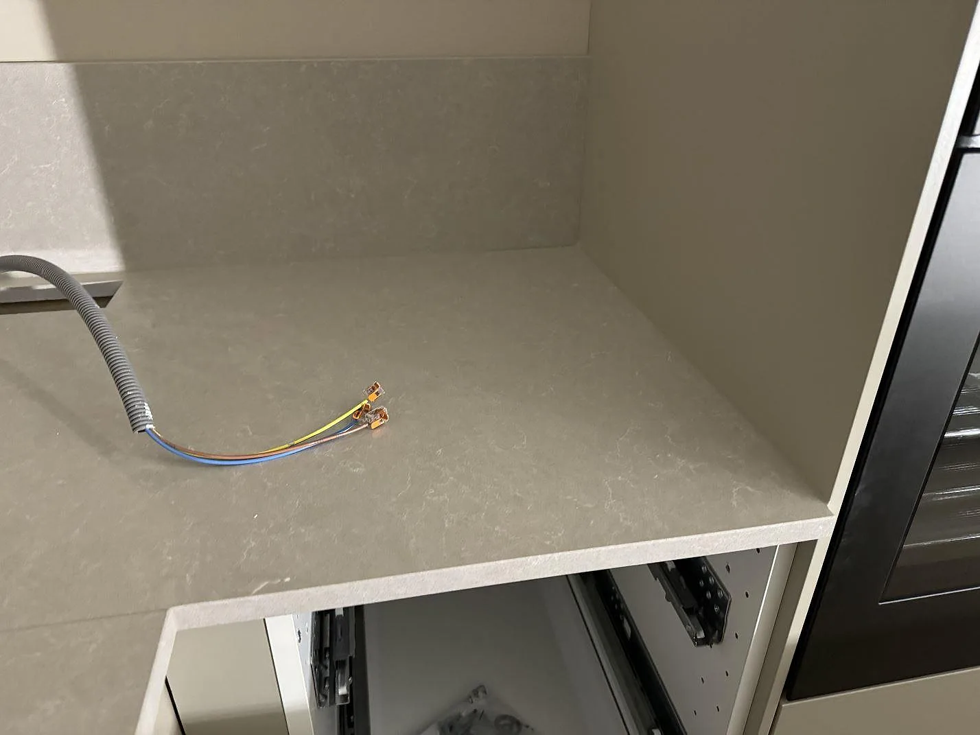 Köksbänkskiva i polerad Technistone Noble Ivory White med stänkskydd och synlig eldragning under montering i Vellinge.