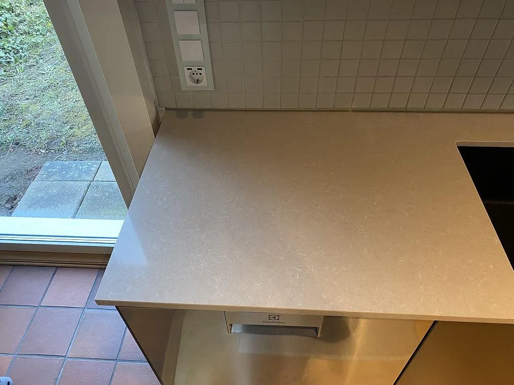 Polerad Technistone Noble Ivory White som köksbänkskiva vid hällen, med ljus komposityta och vitt kakel i ett kök i Vellinge.