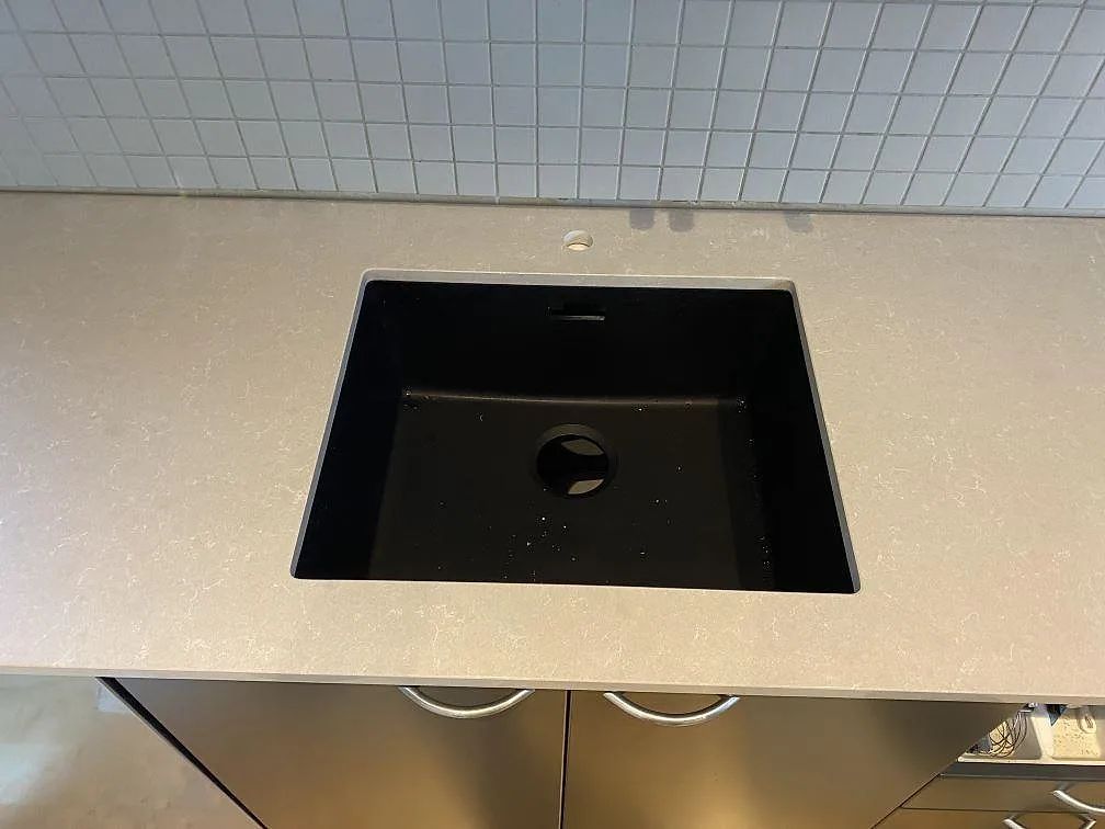 Närbild på svart diskho i en polerad köksbänkskiva av Technistone Noble Ivory White, ljus kvartskomposit, i Vellinge.