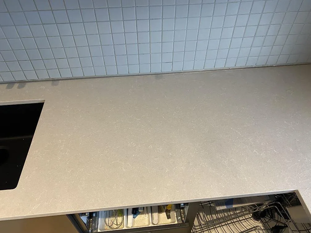 Lång arbetsyta i polerad Technistone Noble Ivory White, ljus kvartskomposit, med diskho i kanten och öppna köksskåp i Vellinge.