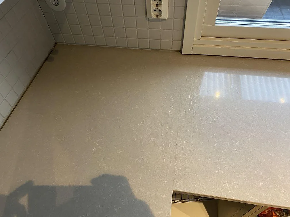 Detalj av den polerade kompositytan Technistone Noble Ivory White på hörnbänken vid fönster och kakel i ett kök i Vellinge.
