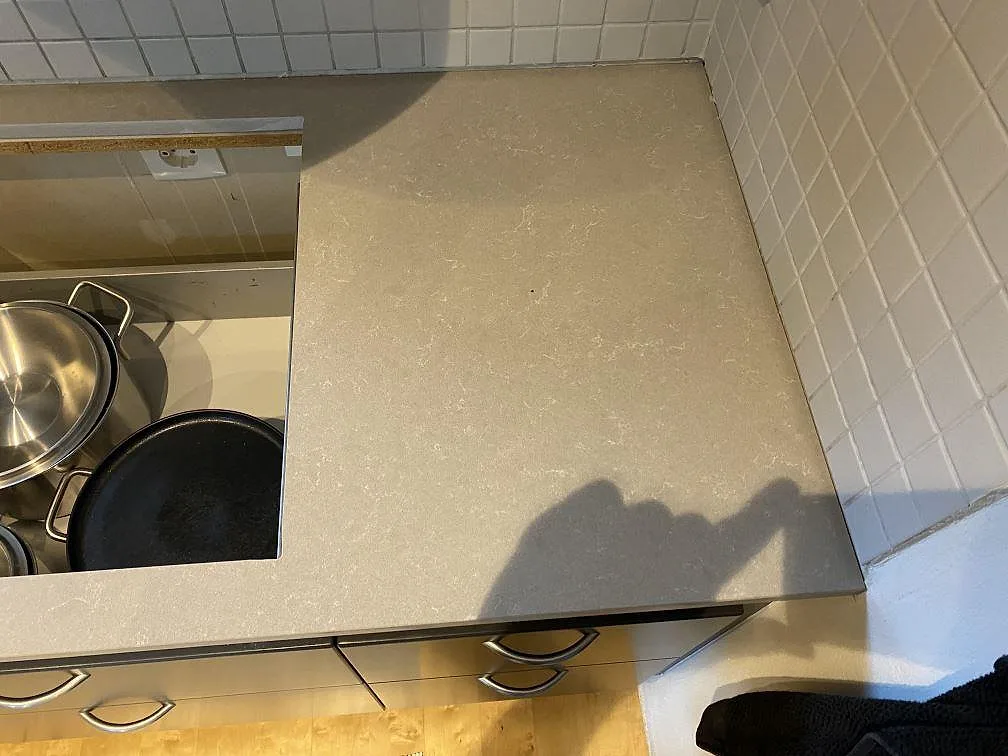 Hörnsektion med polerad Technistone Noble Ivory White som köksbänkskiva, ljus kvartskomposit och vitt kakel i Vellinge.