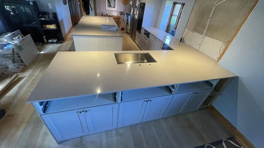 Köksbänkskiva i polerad Technistone Noble Ivory White, komposit, med synlig diskho och köksö under montering i Vellinge.