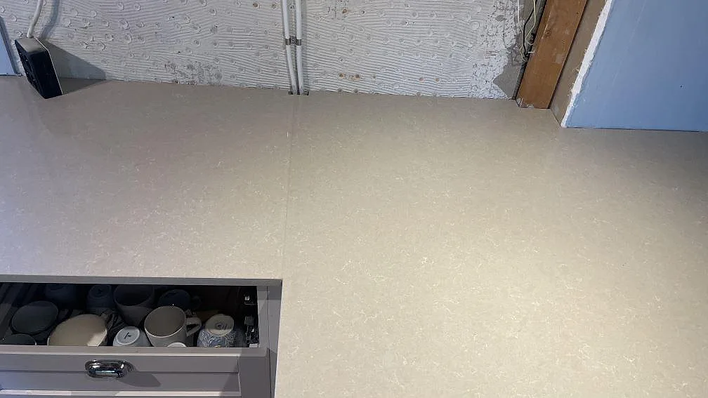 Polerad Technistone Noble Ivory White som arbetsyta längs vägg, kompositbänkskiva under montering i Vellinge.
