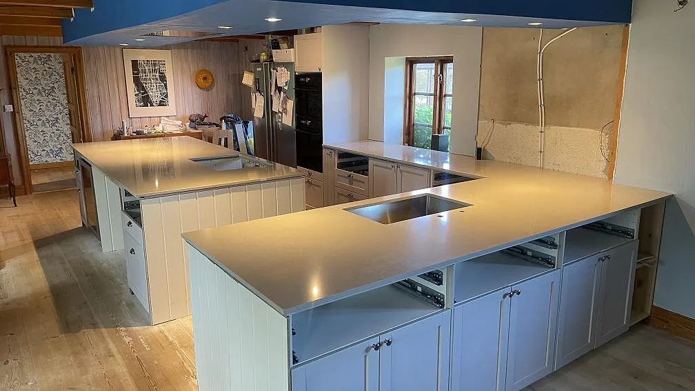 Polerad köksbänkskiva i Technistone Noble Ivory White, komposit, med köksö och väggbänkar i ett kök i Vellinge.