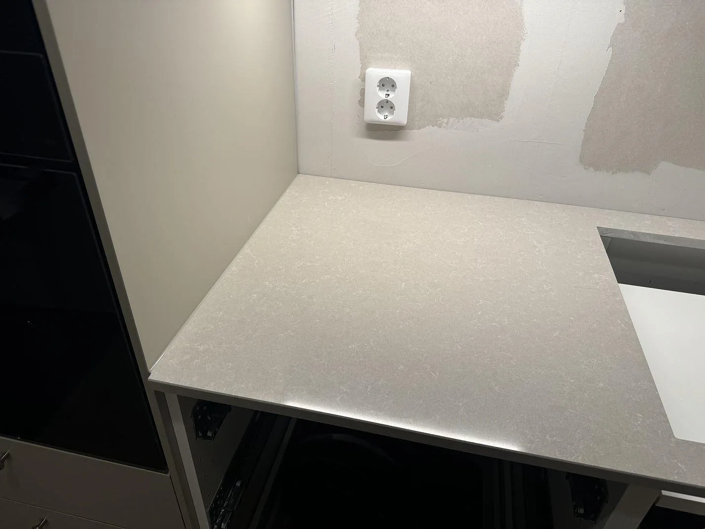 Rak bänkyta i polerad Technistone Noble Ivory White med ljus komposityta, vägguttag och del av hällurtag i Vintrie.