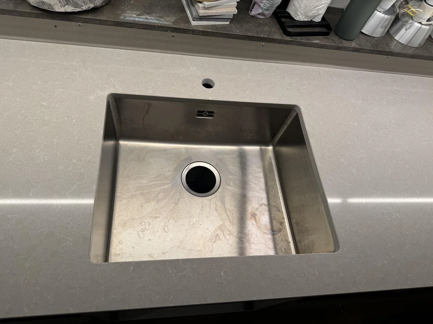 Närbild på rostfri diskho monterad under en polerad bänkskiva i Technistone Noble Ivory White i köket i Vintrie.