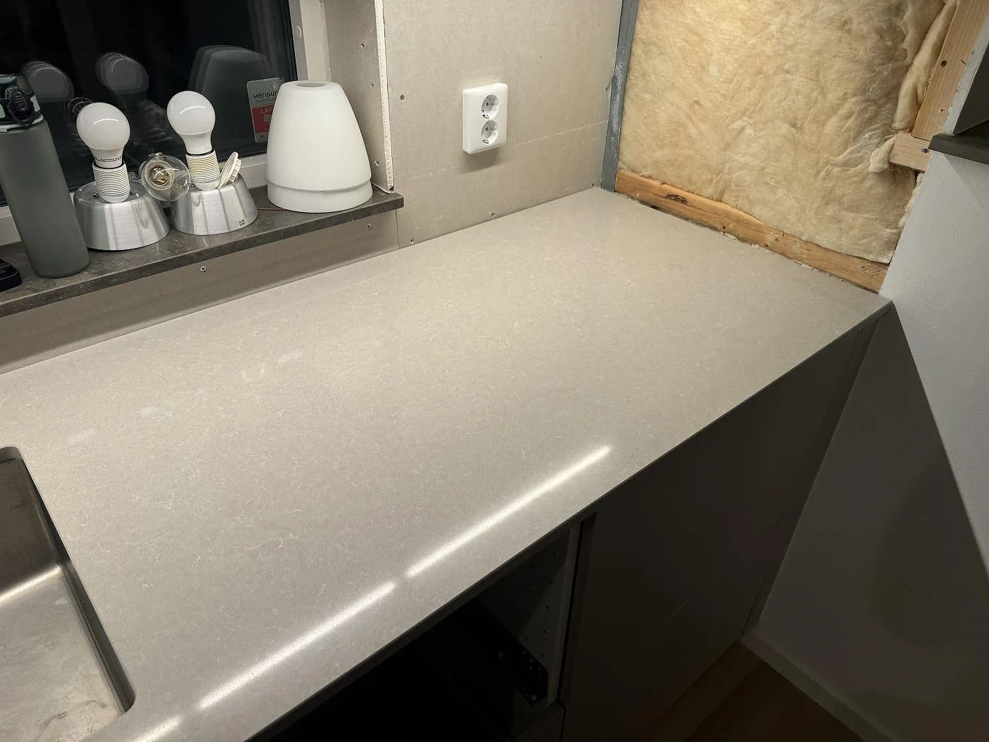 Ljus polerad Technistone Noble Ivory White bänkskiva vid diskhon, med synlig stenyta och vägg under montering i Vintrie.