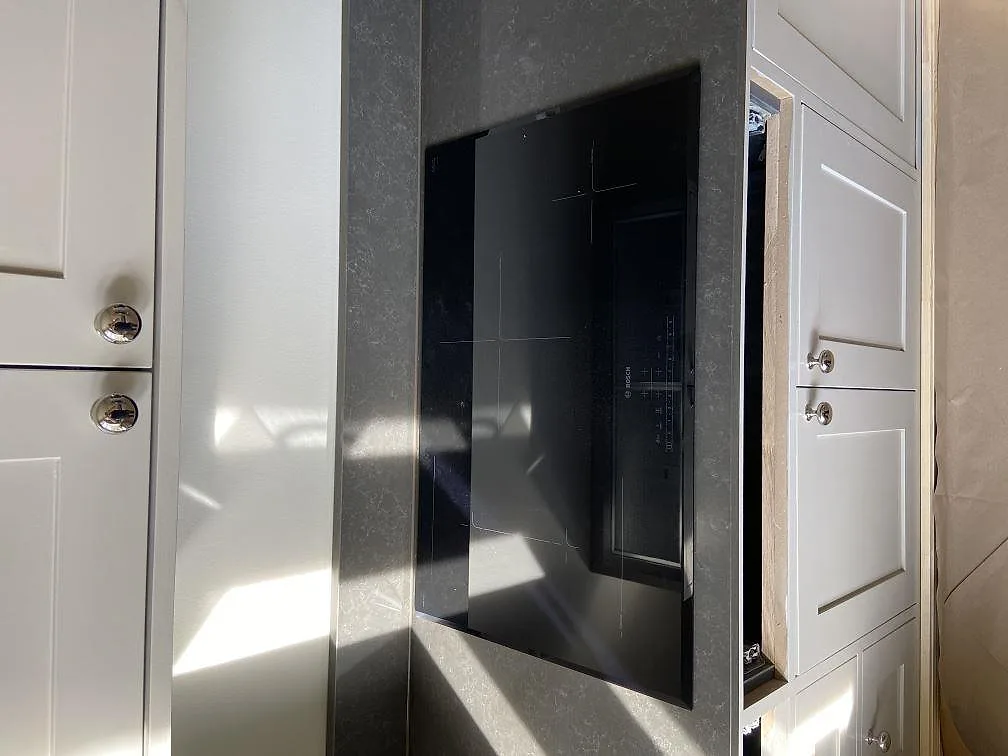 Infälld svart induktionshäll i polerad grå Technistone Noble Pietra Grey-bänkskiva mellan vita köksluckor i ett kök i Göteborg.