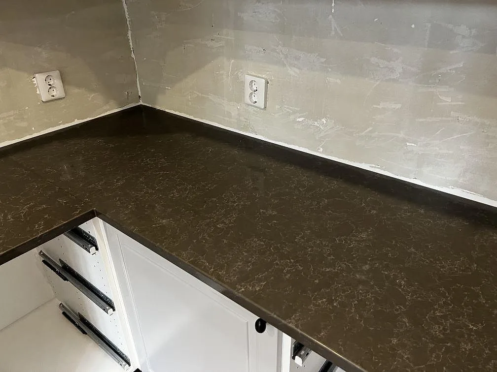 L-formad del av köksbänkskiva i Technistone Noble Pietra Grey med polerad mörkgrå yta i Hästveda.