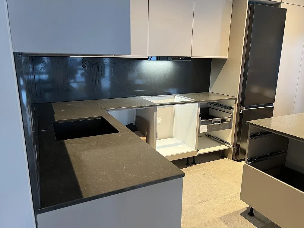 Polerad köksbänkskiva i grå Technistone Noble Pietra Grey, kvartskomposit, längs väggbänkar med mörk väggbeklädnad i ett kök i Ingarö.
