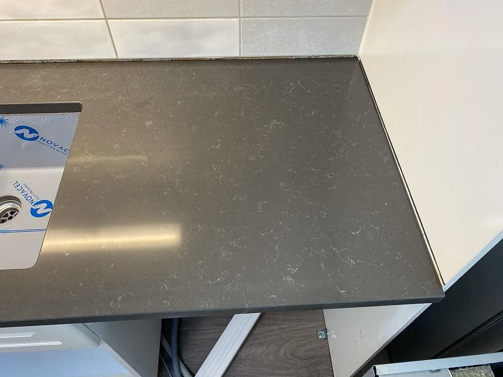 Närbild av polerad Technistone Noble Pietra Grey köksbänkskiva i komposit vid diskhoområdet och väggkaklet i Kungsbacka.