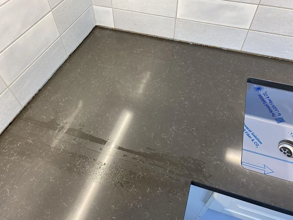 Polerad grå Technistone Noble Pietra Grey komposit med ljusa ådror vid kökets hörn och diskho i Kungsbacka.